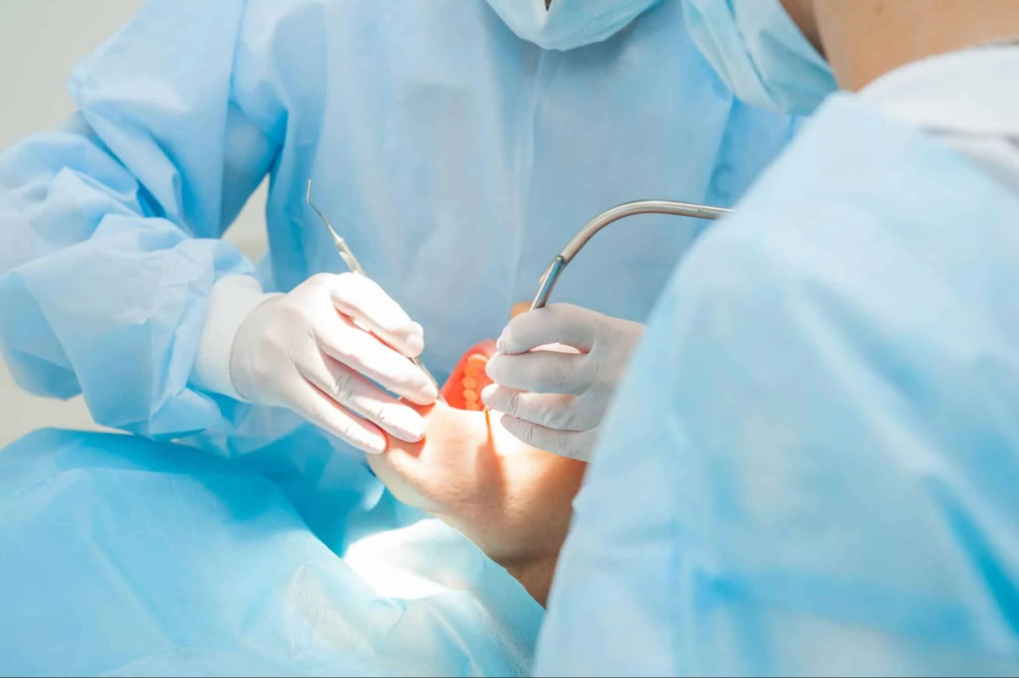 Dentists in blue scrubs performing a clinical surgical procedure on a patient.