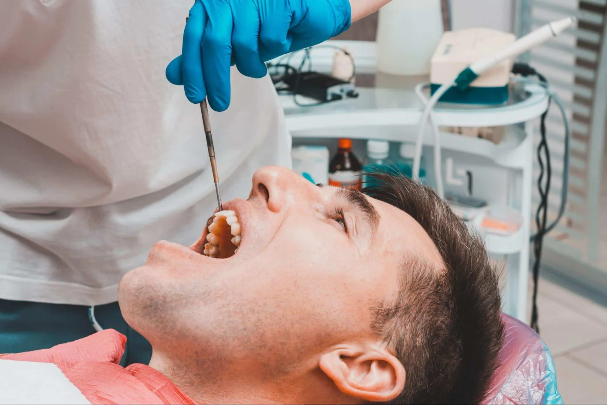 A dentist using a dental tool to examine a male patient's teeth close up